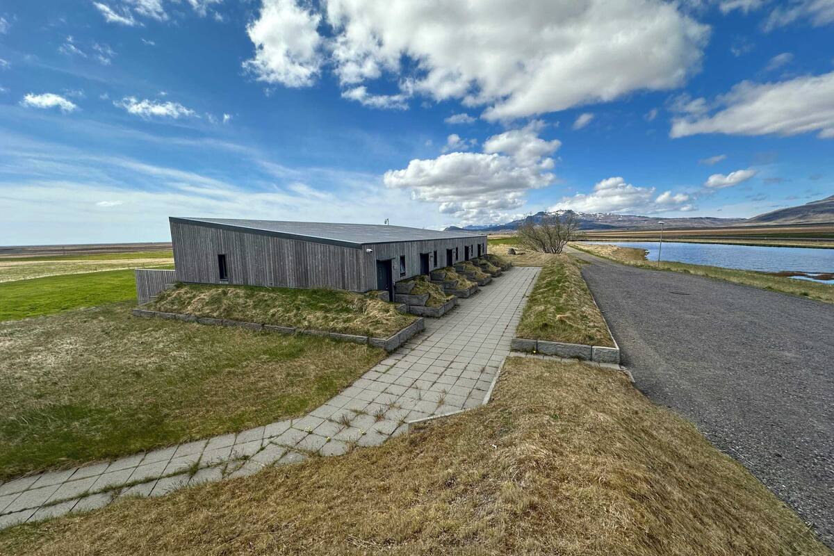 A modern building with a long, straight pathway leading to it, surrounded by grassy areas and a body of water.