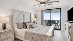 A bedroom with a large bed, a ceiling fan, a nightstand, a dresser, and a balcony with a view. - Serenity Awaits: Unwind in Style with Our Premier Orange Beach Condo Rental (Orange Beach)