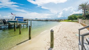A beach with clear water, a dock with boats, and a distant city skyline. - Serenity Awaits: Unwind in Style with Our Premier Orange Beach Condo Rental (Orange Beach)