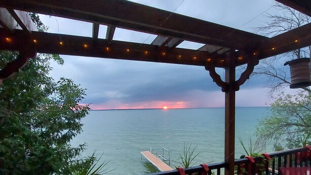 Un muelle de madera con barandilla, con vista a un cuerpo de agua y un atardecer a lo lejos.