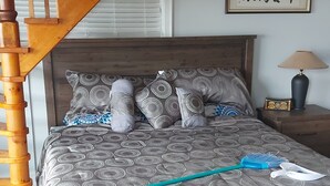 Un dormitorio con cama, escalera de madera, mesita de noche, lámpara y un cuadro en la pared.