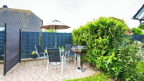 En terrasse med et bord, stole, grill og en stor busk.