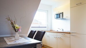 Et moderne køkken med hvide skabe, en mikrobølgeovn og et vindue med skodder.