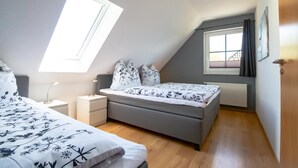 Et soveværelse med skråvæg, en seng med blomstret sengetøj, et sengebord med en lampe og et vindue med gardiner.