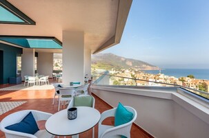 Un balcón con mobiliario de mimbre blanco, una mesita y vistas al mar y al pueblo.