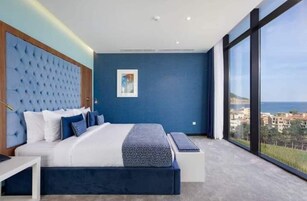 Un dormitorio moderno con una cama grande, cabecera, mesita de noche y vistas al mar a través de amplias ventanas.