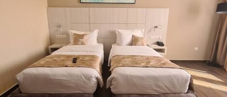 A double room with two beds, a headboard, bedside tables, a lamp, and a painting on the wall.