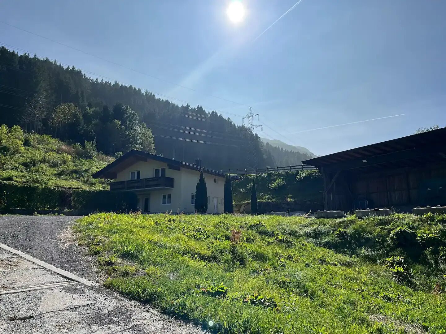 A rural setting with a house and a barn, surrounded by greenery and hills.