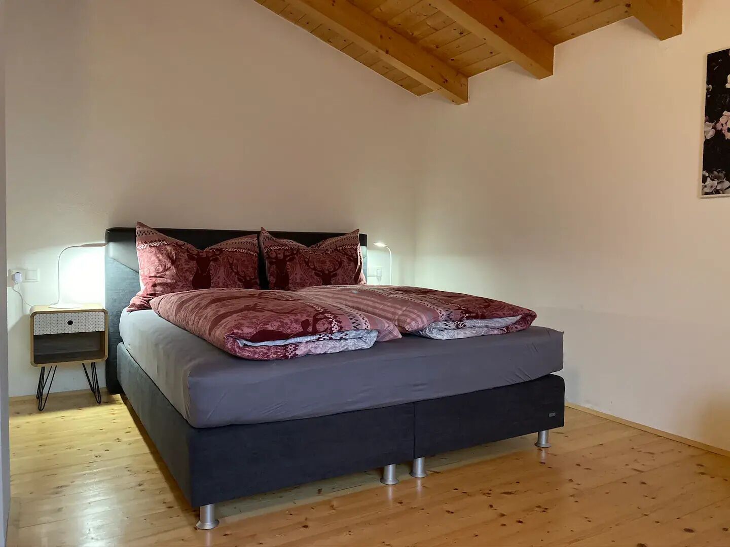 A bedroom with a bed, wooden floor, and a ceiling with exposed beams.
