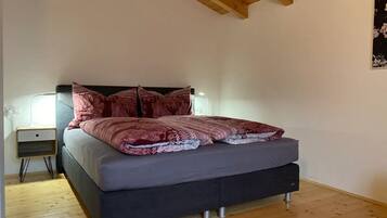 A bedroom with a bed, wooden floor, and a ceiling with exposed beams.