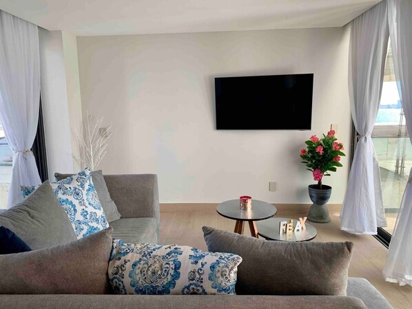 A modern living room with a grey sofa, a small round table with a red candle, and a potted plant with pink flowers.