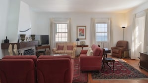 A living room with red sofas, a television, a fireplace, and a large window with curtains. - On the North Coast, by the sea - Casa do Terreiro (São Vicente)