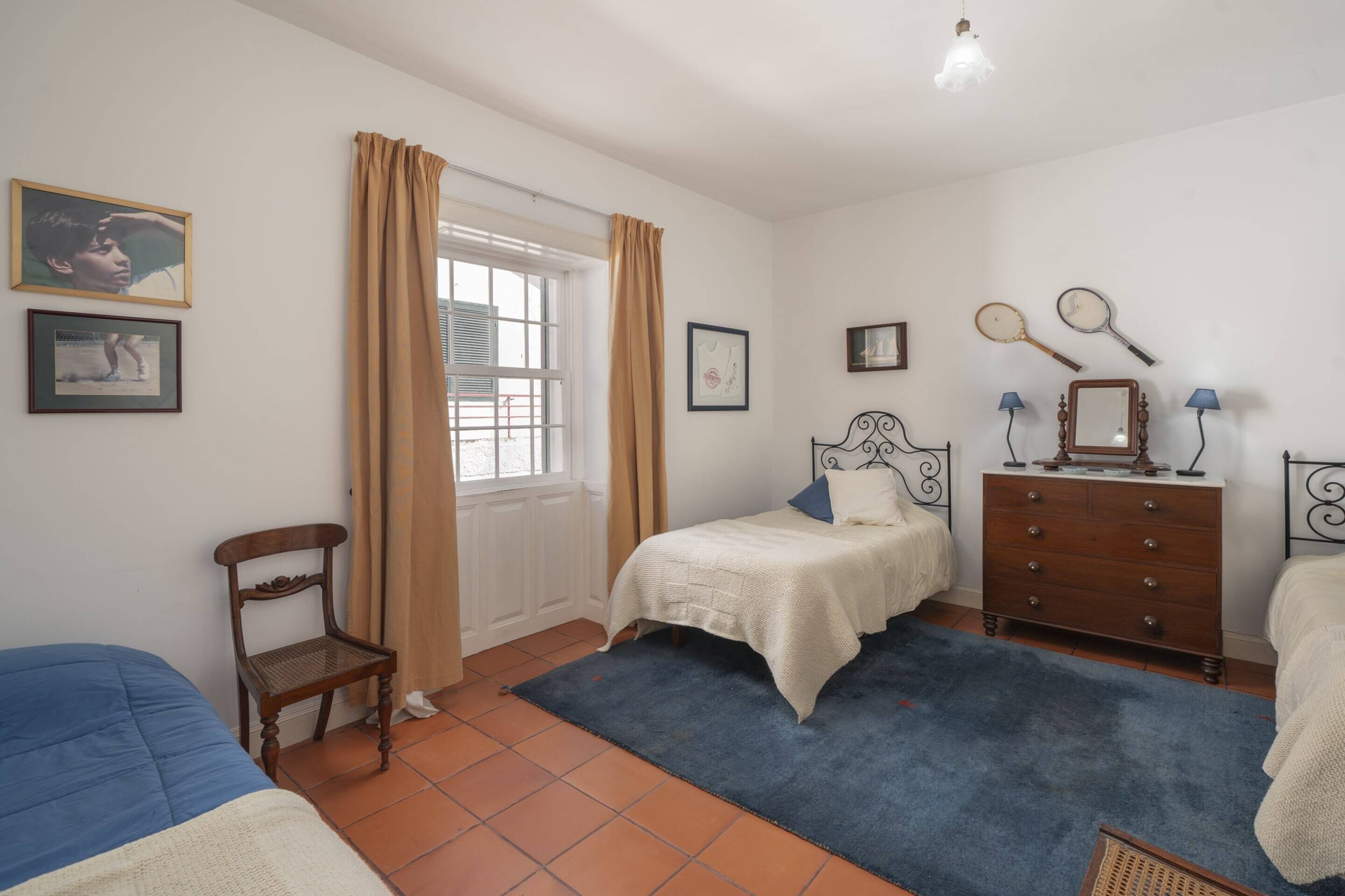 Een slaapkamer met een bed, een dressoir, een stoel en een raam met gordijnen.