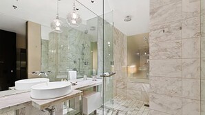 A modern bathroom with two sinks, a glass shower enclosure, and marble flooring.