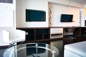 A modern living room with a glass coffee table, white sofas, and a flat-screen TV mounted on the wall.