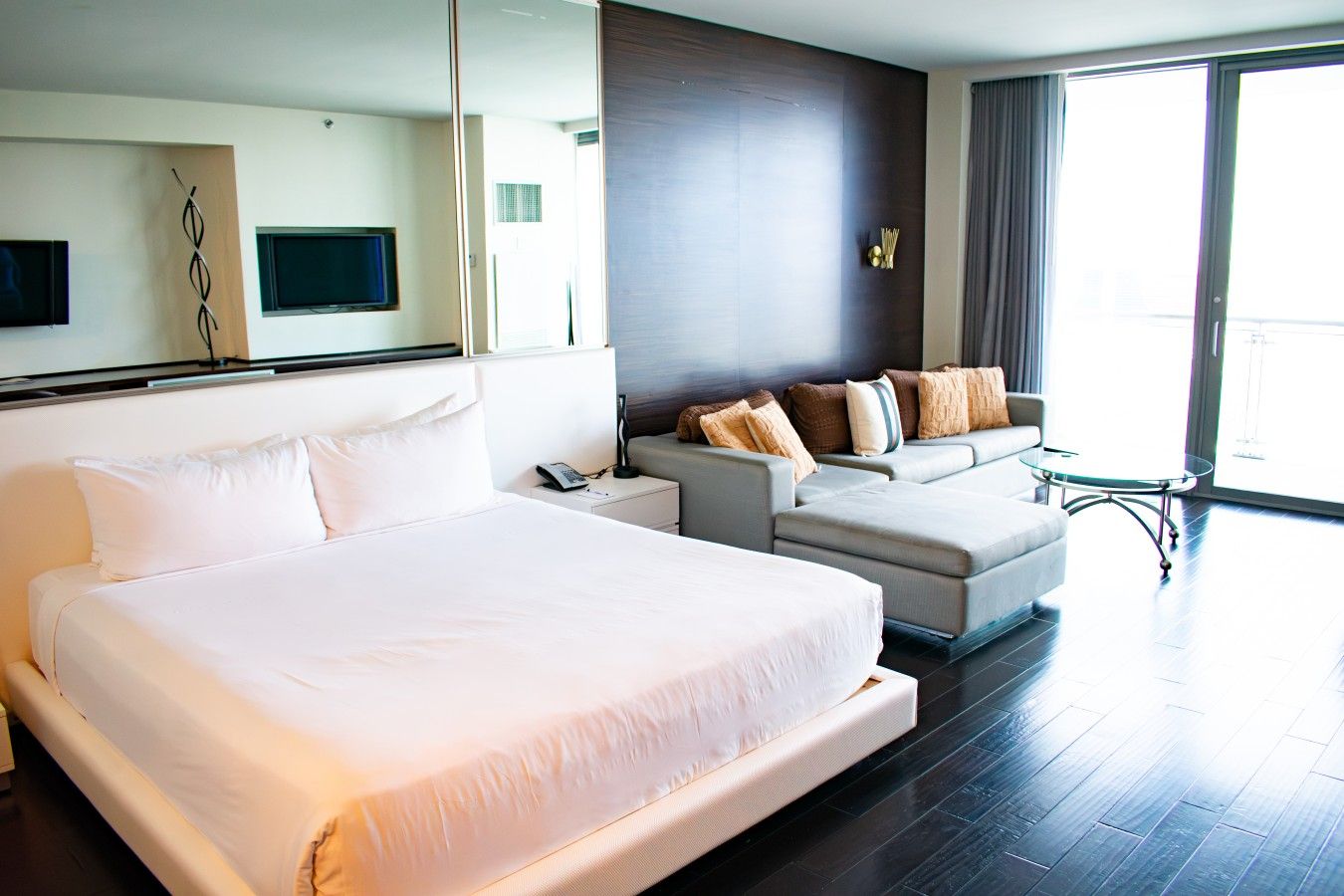 Habitación de hotel con una cama grande, un sofá, una mesita pequeña y un televisor montado en la pared.