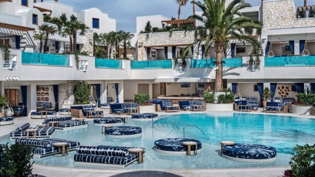 A pool area with lounge chairs and a circular seating area, surrounded by multi-story buildings with balconies and palm trees.