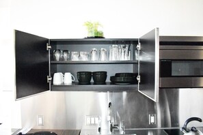 A kitchen with a stainless steel range hood, a sink, and a cabinet with shelves holding various kitchenware. - Palms Place Hotel StripView (Las Vegas)