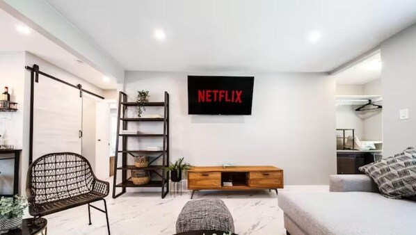 Una sala de estar moderna con un sofá, una mesa de centro, un televisor montado en la pared, un mueble de madera y una silla metálica negra.