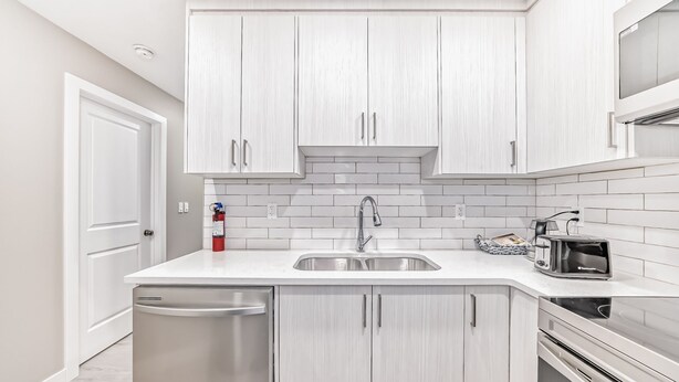 Cocina moderna con muebles blancos, pileta de acero inoxidable y microondas integrado.