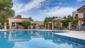 Une piscine entourée d’une clôture et d’arbres, avec des chaises longues et des parasols.