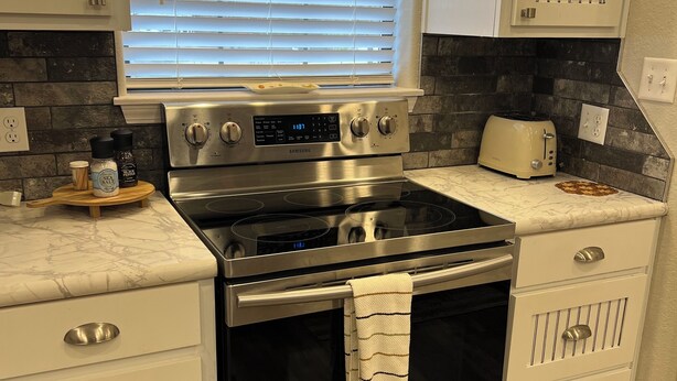 A modern kitchen with a stainless steel stove, a toaster, and a window with blinds. - Tranquil 3-bedroom barn right next to Lake Tenkiller in Vian with WiFi, AC (Vian)