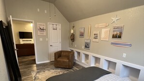 Une chambre à coucher avec un lit, un ventilateur de plafond, une porte, une chaise et un mur orné de tableaux.