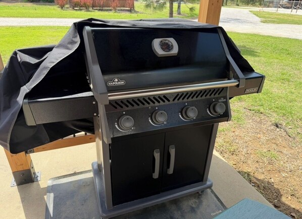 Una parrilla exterior negra con cuatro quemadores y un termómetro digital, ubicada sobre una superficie de concreto.