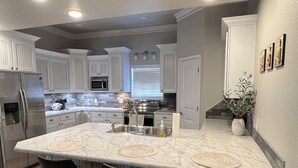 A modern kitchen with white cabinetry, a central island with bar stools, a stainless steel refrigerator, and a built-in oven. - Tranquil 3-bedroom barn right next to Lake Tenkiller in Vian with WiFi, AC (Vian)