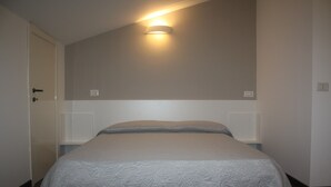 Un dormitorio con cama, una puerta y una lámpara fijada a la pared.