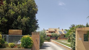 Una entrada cerrada a una propiedad llamada 'Desert Orizzonti', con un camino de entrada pavimentado que conduce a un edificio con tejado de baldosas y paredes de ladrillo.