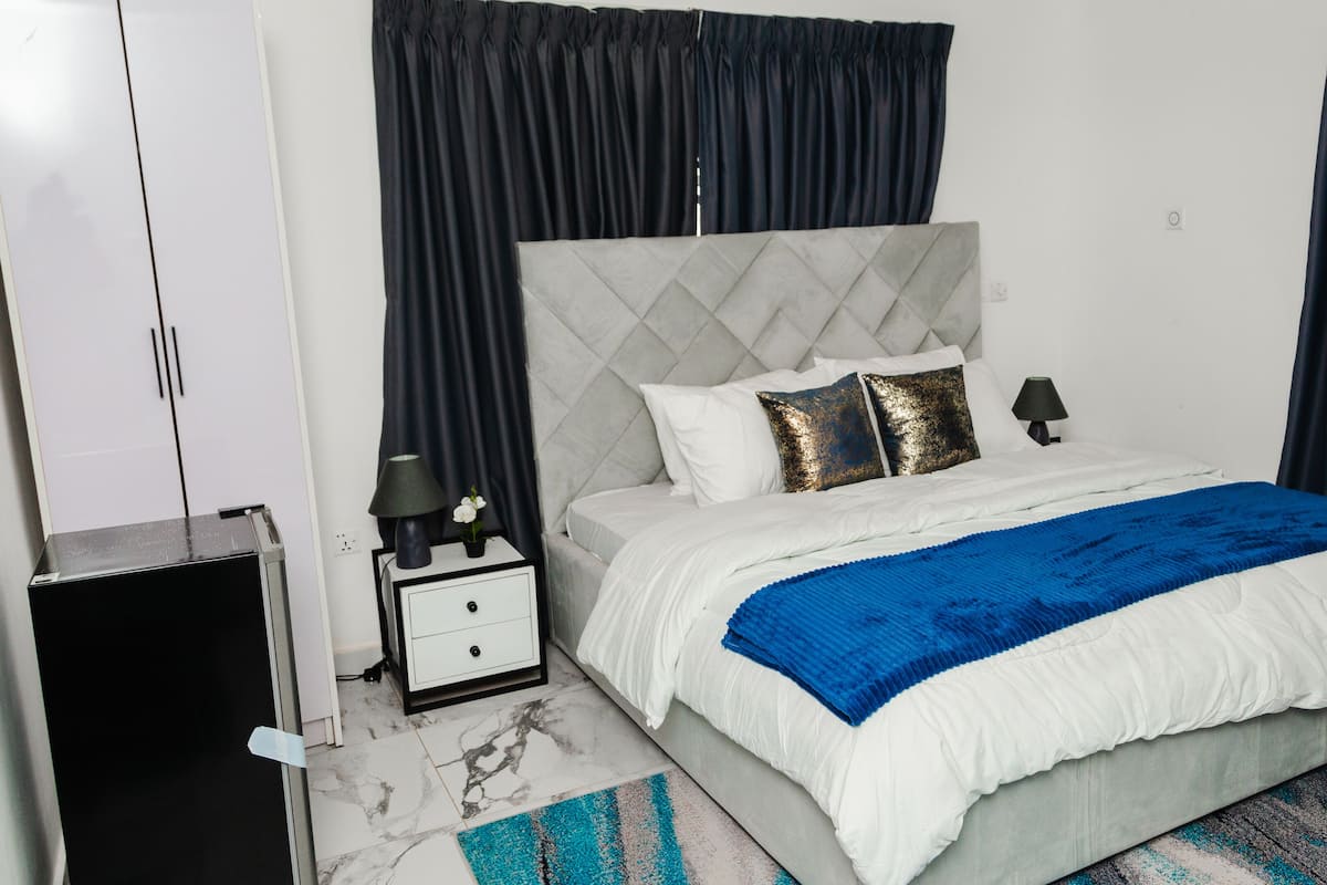 A bedroom with a bed, nightstand, lamp, and curtains.