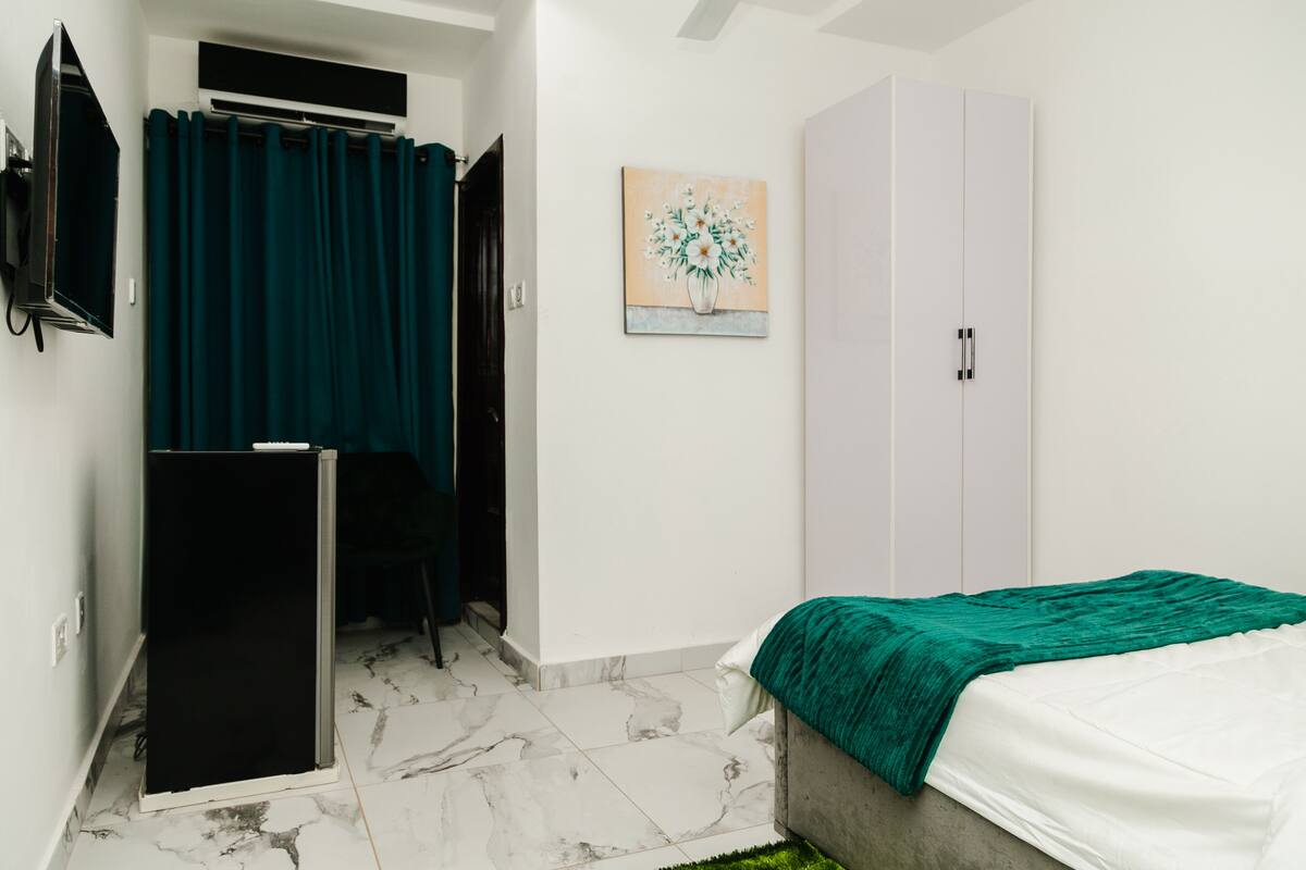 A bedroom with a bed, a wardrobe, a television, and a painting on the wall.