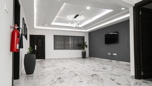 A spacious room with a marble floor, a ceiling fan, recessed lighting, a large potted plant, and a mounted TV. - Sunrise Cave Guest House (Oyibi)