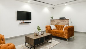 A modern living room with a flat-screen TV mounted on the wall, a wooden coffee table with decorative items, a tufted orange sofa, and a minimalist wooden cabinet. - Sunrise Cave Guest House (Oyibi)