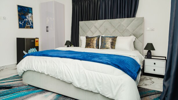 A bedroom with a bed, nightstand, wardrobe, and artwork on the wall. - Sunrise Cave Guest House (Oyibi)