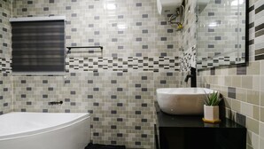 A modern bathroom with a freestanding bathtub, a large mirror, and a sink with a potted plant. - Sunrise Cave Guest House (Oyibi)
