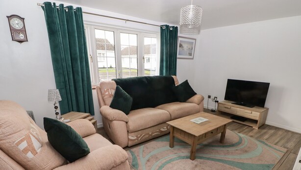 A living room with a sofa, armchair, coffee table, TV, and a window with curtains. - 13 Gower Holiday Village (Swansea)