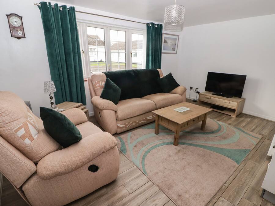 A living room with a sofa, armchair, coffee table, TV, and a window with curtains.