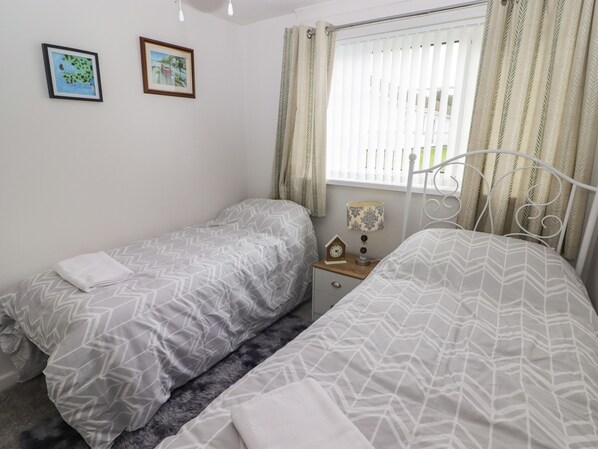 Une chambre avec deux lits simples, une table de chevet, une lampe et deux tableaux encadrés au mur.