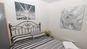 A neatly made bed with striped bedding, a globe, and a clock on a bedside table. - 13 Gower Holiday Village (Swansea)