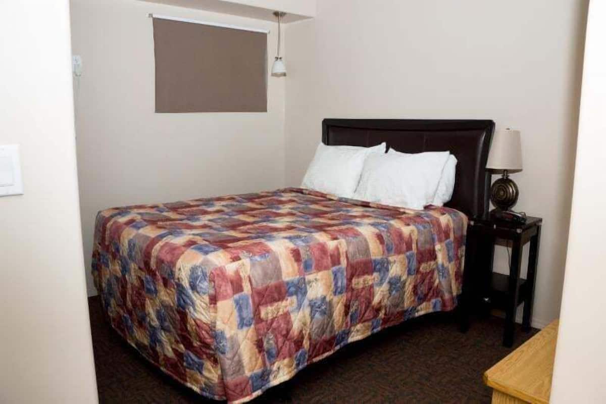 A hotel room with a bed, a nightstand, a lamp, and a window with a blind.