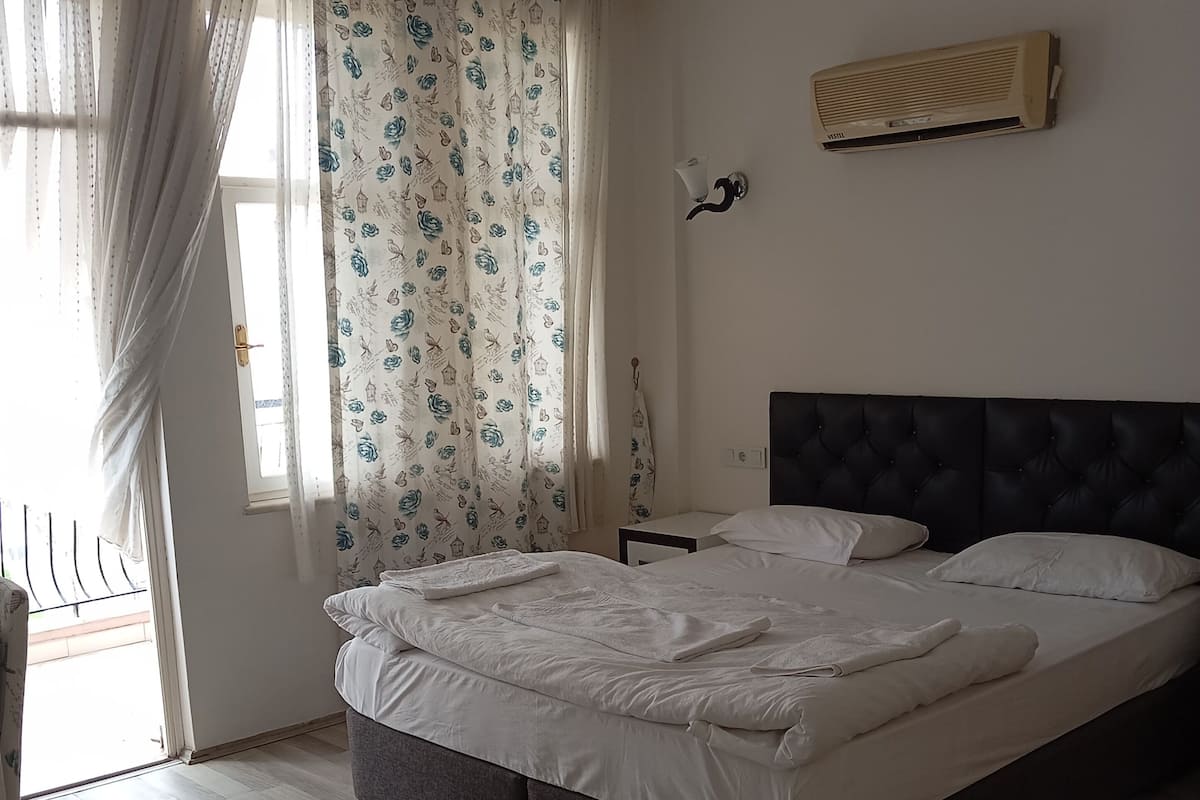 A bedroom with a large bed, a wardrobe, a window with curtains, and a wall-mounted air conditioner.