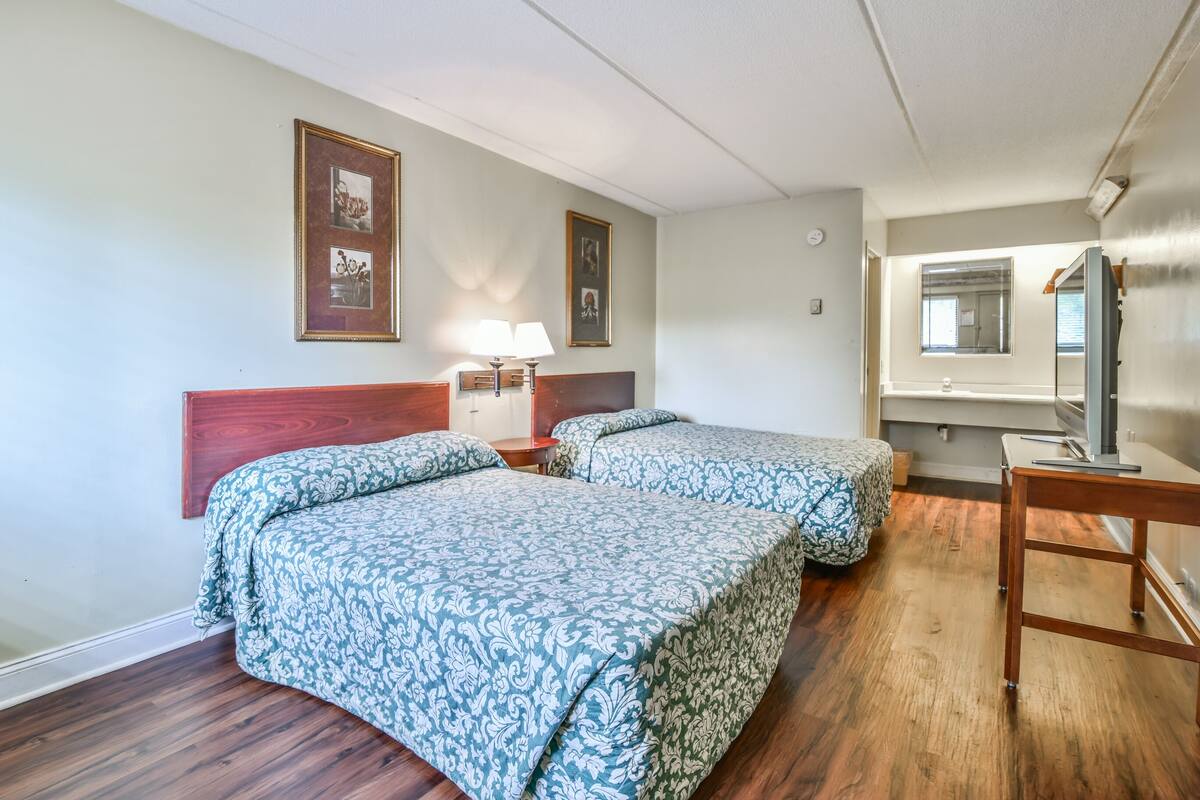 Hotelkamer met twee bedden, een houten hoofdeinde, nachtkastjes met lampen, een spiegel en een houten bureau.