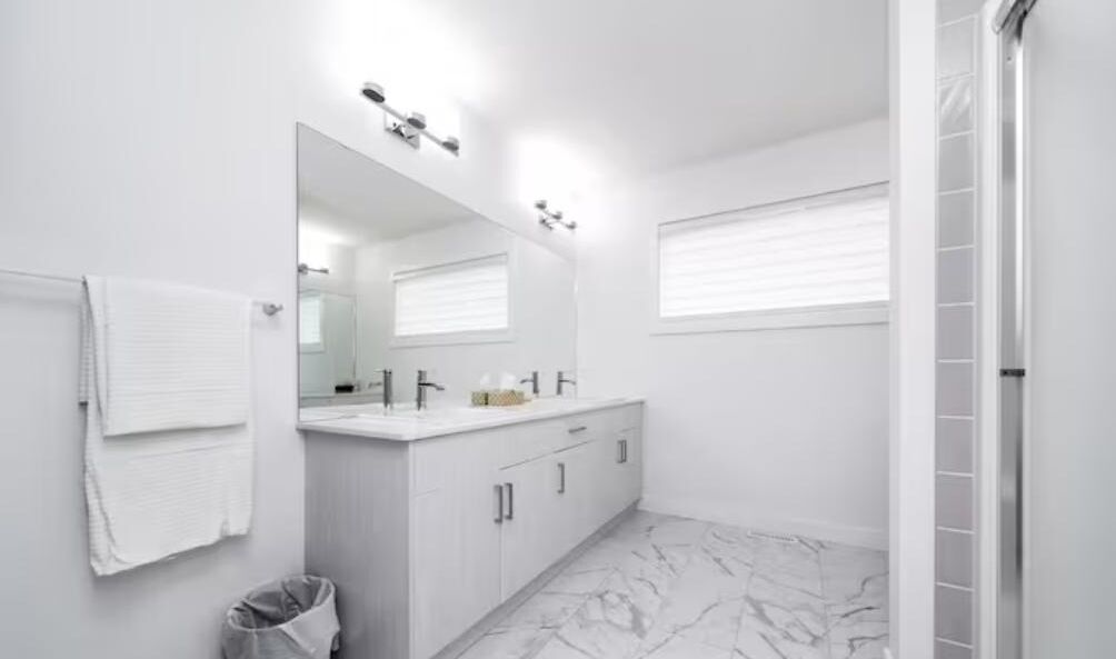 A modern bathroom with a large mirror, white cabinetry, and a marble floor.