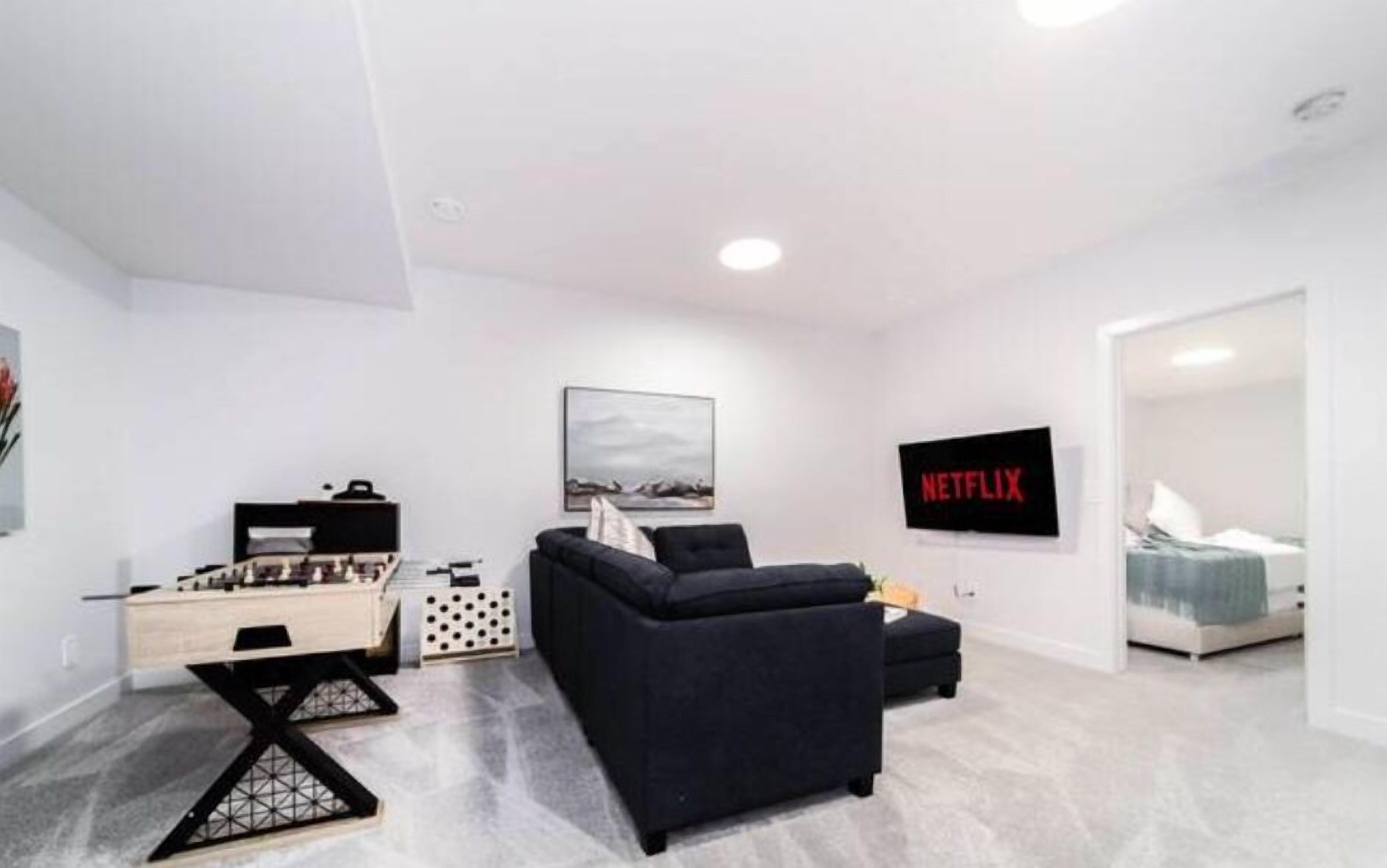 Ein modernes Wohnzimmer mit Sofa, Schreibtisch und Bücherregal. An der Wand hängt ein Gemälde und ein Schild mit der Aufschrift 'NETFLIX'.