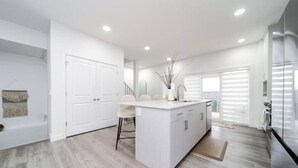 A modern kitchen with white cabinetry, a central island, and a dining area with chairs.