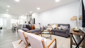 A spacious living room with a grey sofa, a coffee table, and a TV on a wooden stand.