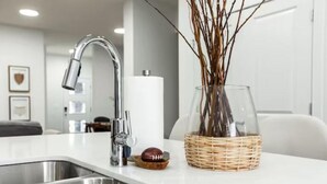 A modern kitchen with a stainless steel sink, a chrome faucet, and a glass vase with branches.