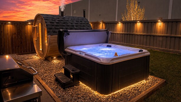 A hot tub and sauna in a backyard with a wooden fence and a building in the background.
